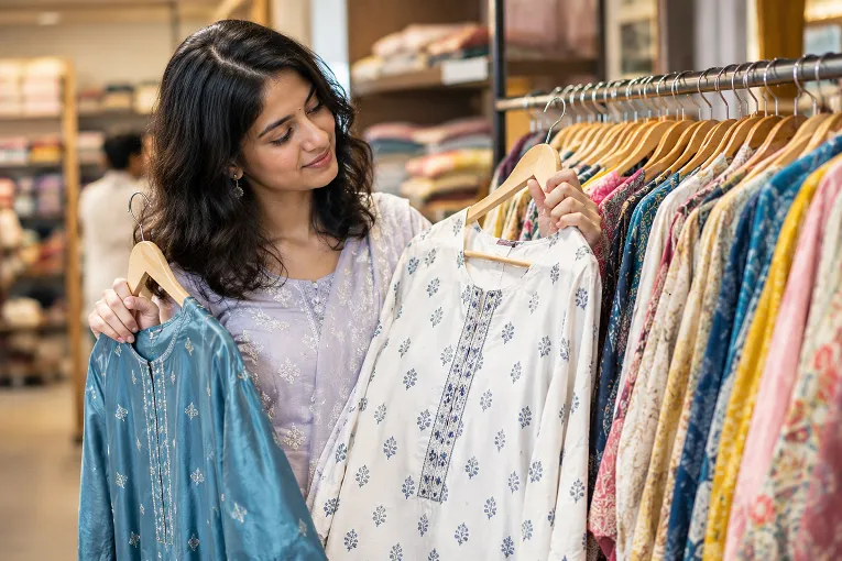 Woman comparing cotton vs rayon vs viscose fabric kurtis on a shop rack in Surat
