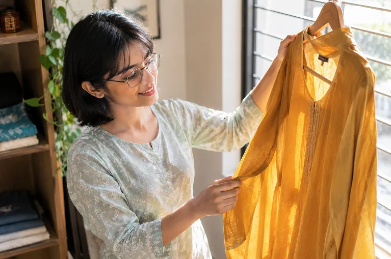 Woman hanging a viscose kurta on a wooden hanger to dry in the shade after a gentle wash
