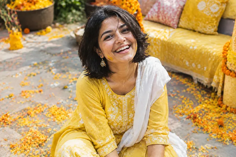 Woman in a yellow cotton kurta set laughing at a haldi ceremony