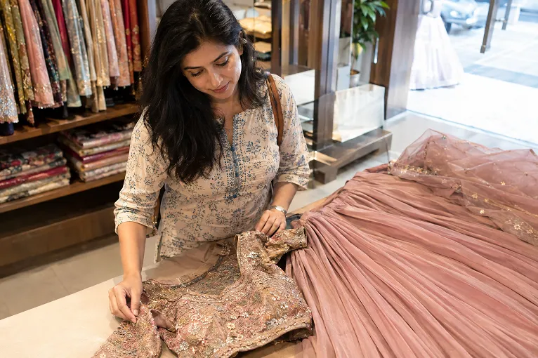 Woman comparing a lehenga blouse, skirt and dupatta on a showroom counter to split her budget