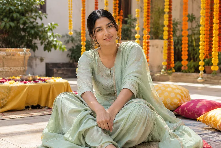 Woman in a soft cotton silk sharara set seated on a floor cushion at a mehndi function