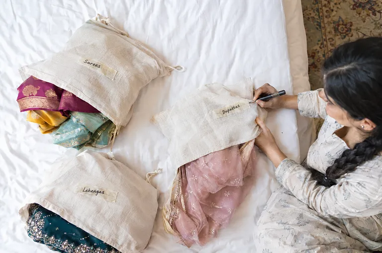 Three labelled cotton bags on a hotel bed keeping clean and worn wedding outfits apart