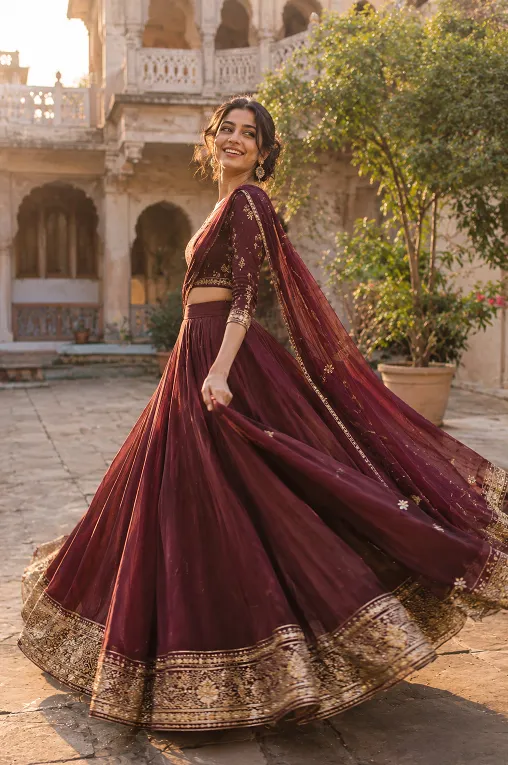 Woman twirling in a deep wine lehenga with a gold border at a wedding courtyard