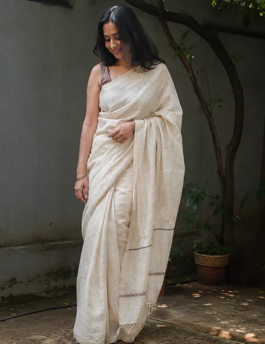 Woman wearing a natural off-white linen saree outdoors in dappled sunlight, a breathable summer saree fabric for India