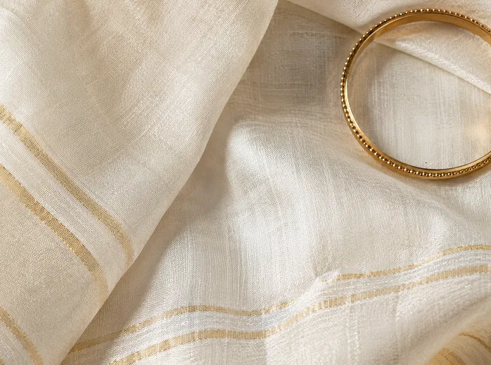 Off-white chanderi cotton fabric texture showing subtle sheen and weave detail with a gold bangle for kurta styling