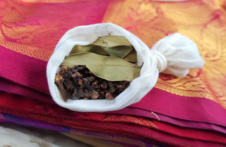 Muslin pouch with cloves and neem leaves placed on folded silk saree for storage protection