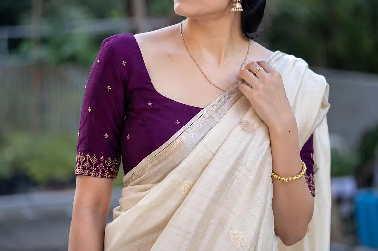 Close-up of a woman wearing a cream ivory saree paired with a deep jewel-toned blouse, demonstrating an elegant Indian ethnic wear colour combination in natural daylight.