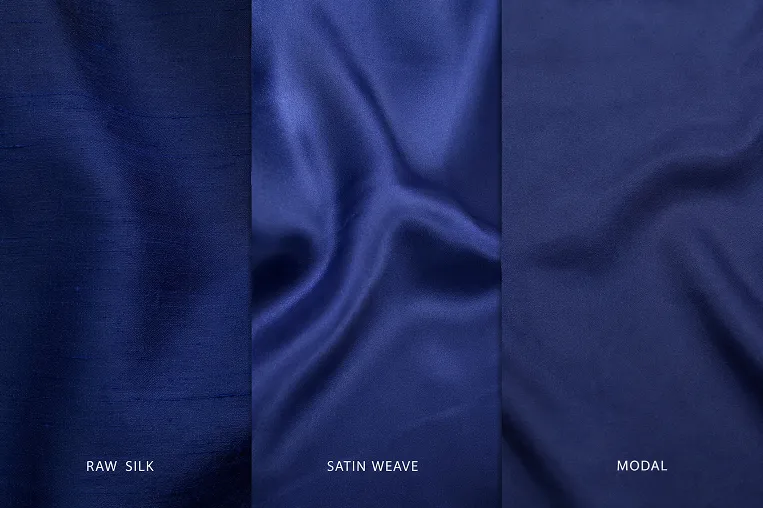 Studio comparison of deep blue fabric swatches in raw silk, satin weave, and modal, showing how the same colour appears differently across Indian ethnic wear fabrics under consistent lighting.