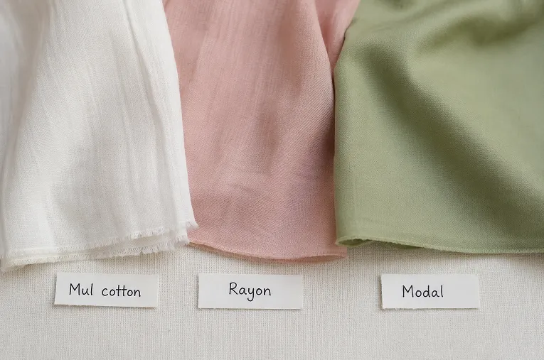 Flat lay comparison of mul cotton, rayon, and modal fabric swatches showing texture and drape differences for plain kurtas