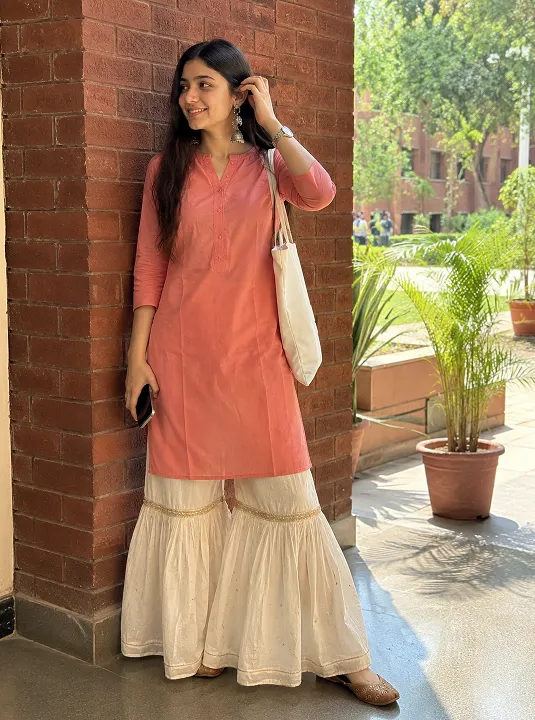 Student wearing a plain coral kurta with a white sharara and juttis on a college campus