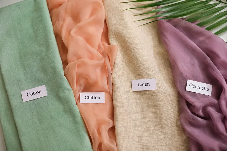 Flat lay of summer saree fabric swatches including cotton, chiffon, linen and georgette in soft pastel colors