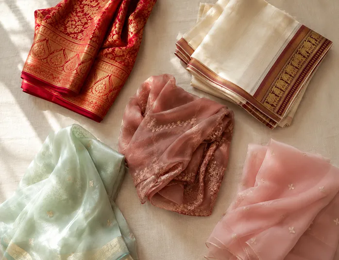 Types of sarees in India including Banarasi silk, Chettinad cotton, georgette, Chanderi and chiffon arranged as a flat lay in natural window light