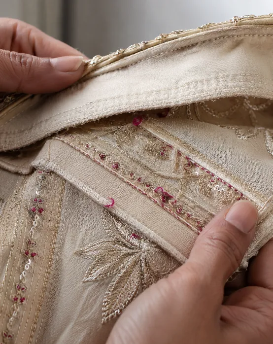 Close up of hands inspecting the inside seam, lining, and embroidery thread work of a lehenga skirt to check stitching quality before purchase.