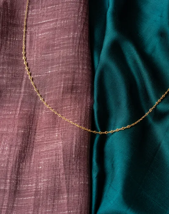 Handloom cotton and plain silk saree fabric texture compared with gold chain necklace