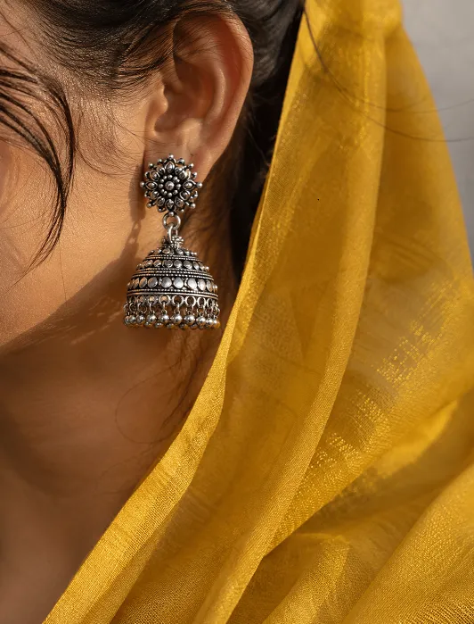 Oxidised silver jhumka earring against plain mustard georgette saree pallu