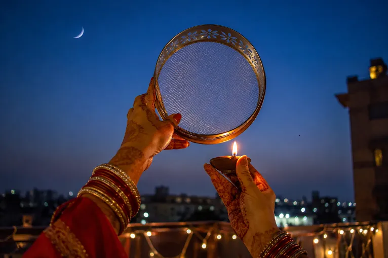 Hands raised with sieve and diya during karva chauth moon sighting ritual