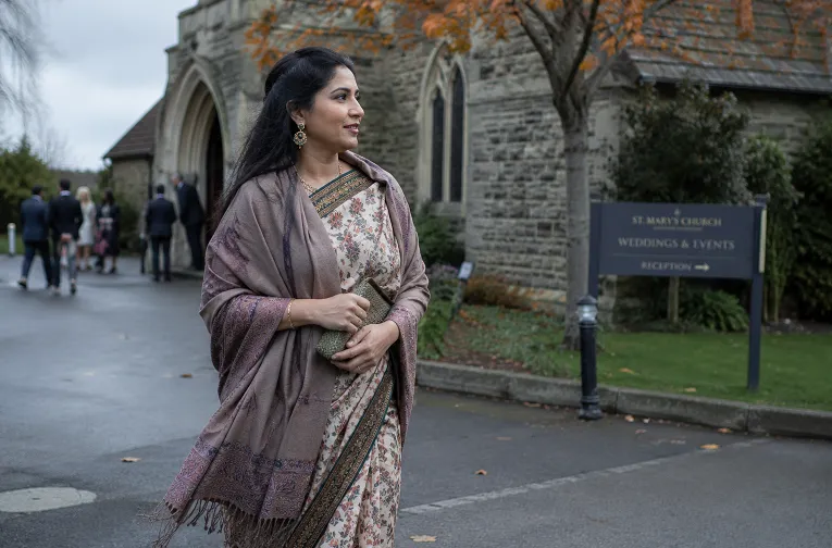 Indian woman layering a shawl over her saree outside a British wedding venue in cool autumn weather
