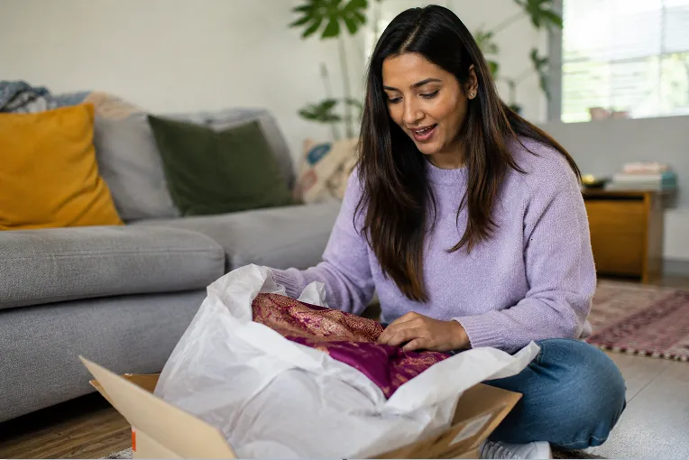 Indian woman unboxing an online saree order at home in the UK, checking fabric against the listing photo
