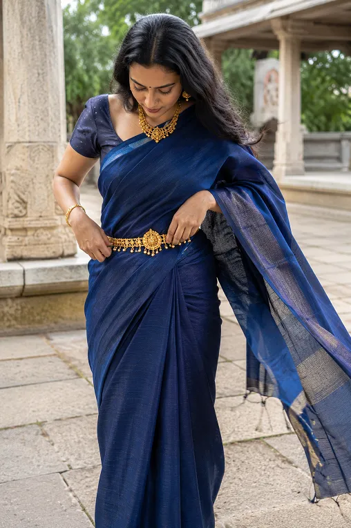 Woman adjusting gold waist belt over plain silk saree while walking