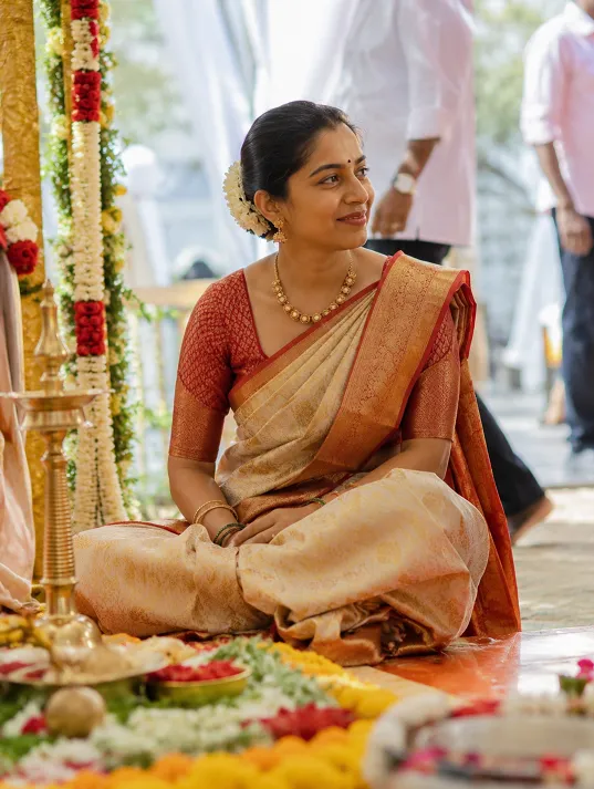 Indian woman seated near a decorated wedding mandap wearing a traditional silk saree with the pallu draped over one shoulder during an outdoor wedding ceremony.