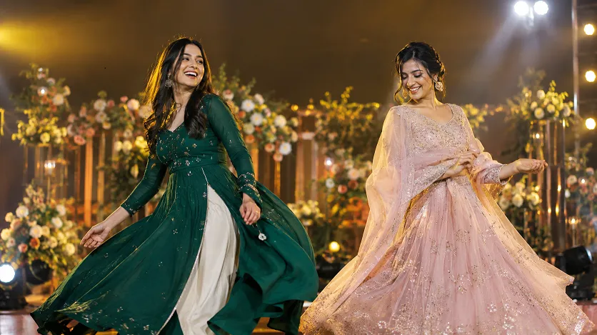 Two women dancing in a lehenga and an Anarkali on a sangeet dance floor to compare lehenga vs anarkali for sangeet